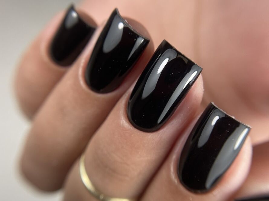 A close-up view of a hand with short, glossy black gel nails, showing smooth, even surfaces and sharp shine reflections.