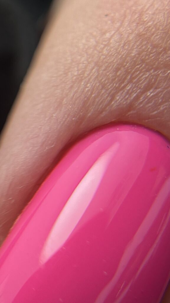 Extreme close-up of a bright pink gel nail with a smooth, glossy surface near the cuticle.