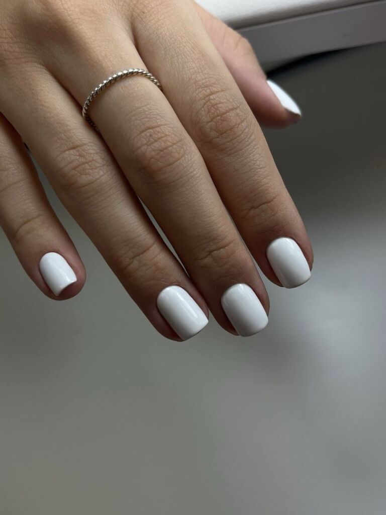 Short square white gel nails with a glossy finish, done using the Russian manicure technique.