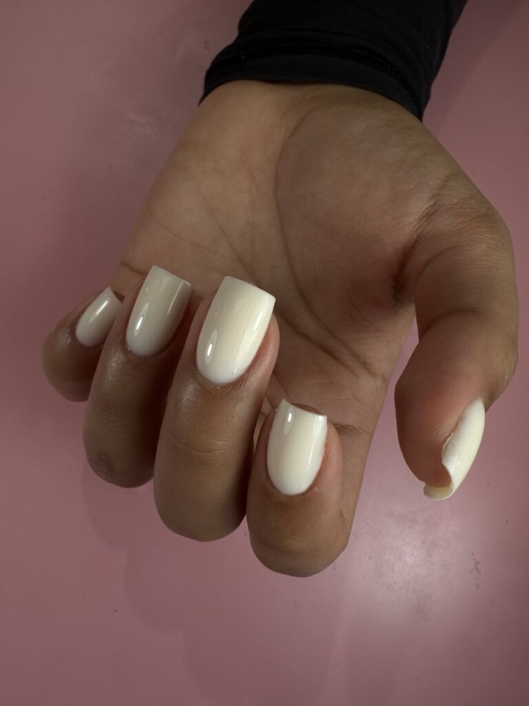 Short square milky white gel nails with a smooth, glossy finish on a hand.
