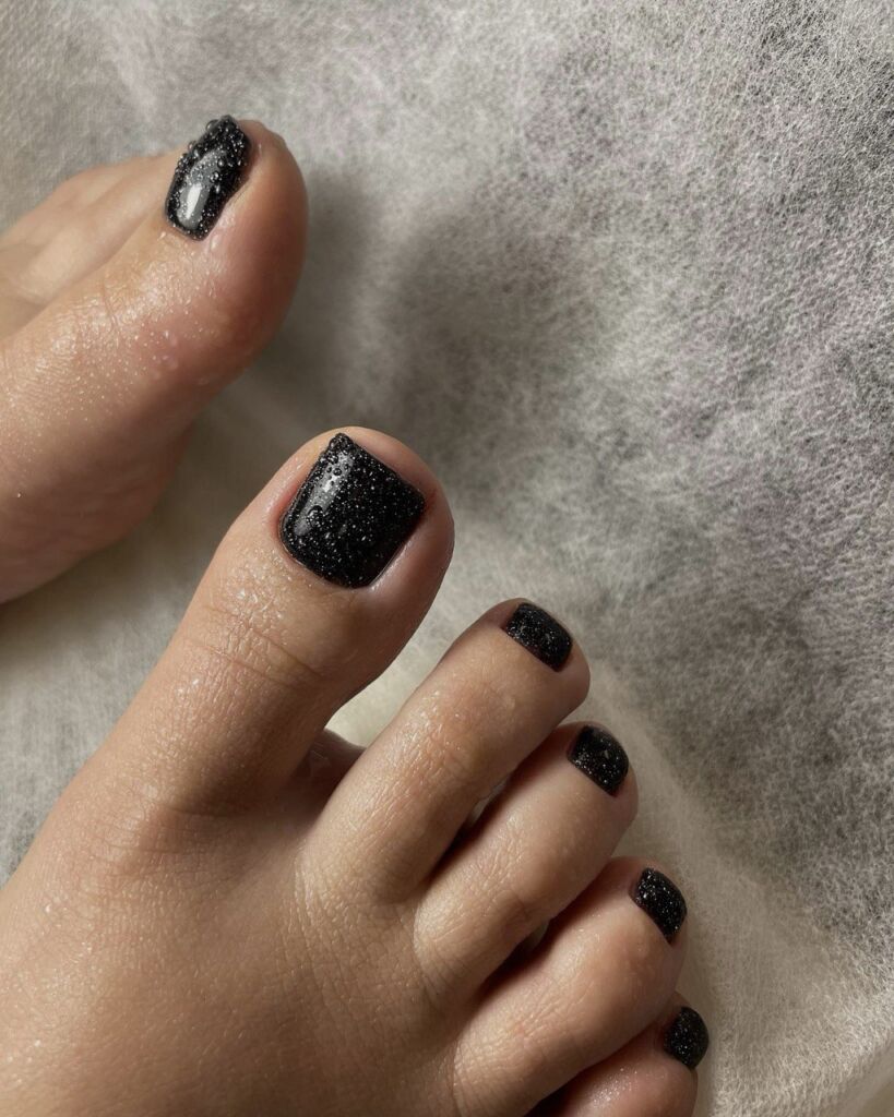 Short square black gel toenails with a glossy finish, done using the Russian pedicure technique.