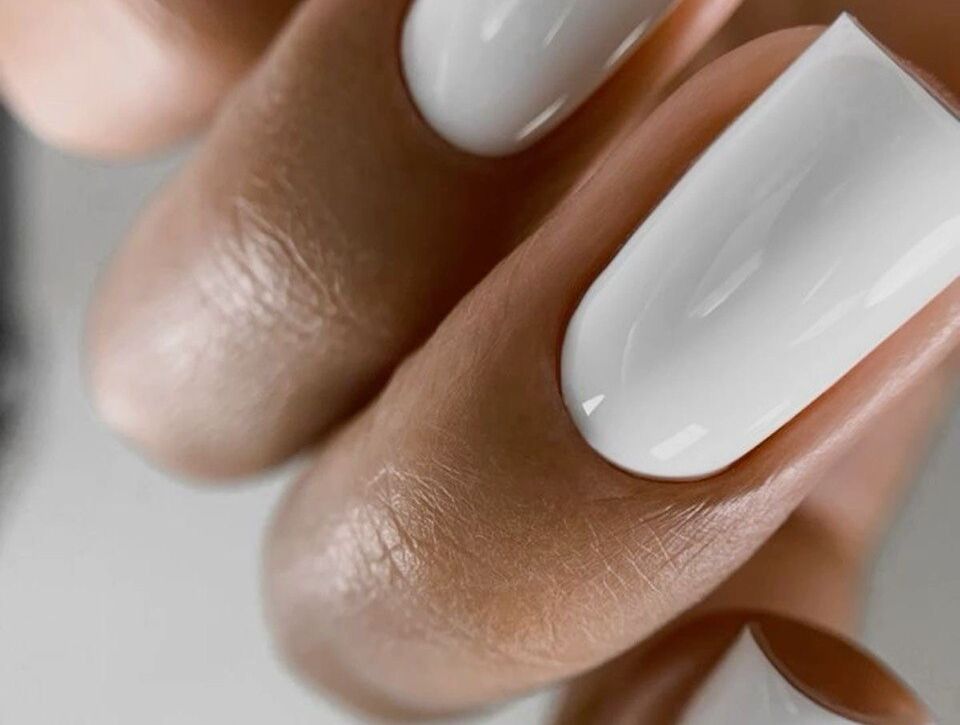 Close-up of a hand with long square-shaped nails coated in a solid opaque white high-gloss polish, styled as a sleek and elegant bridal manicure against a soft light background.