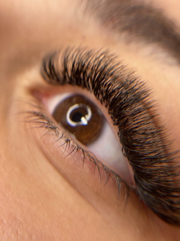 Close-up of brown eye with dramatic black volume lash extensions showing dense, wispy fan pattern and natural lower lashes