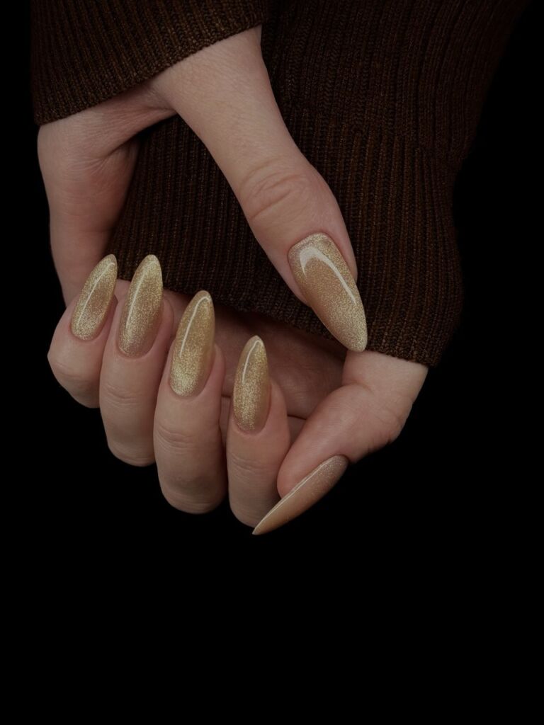 Long almond-shaped gold shimmer gel nails with a smooth finish, done using the Russian manicure technique.