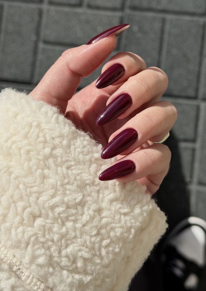 Long almond-shaped burgundy gel nails with a glossy finish, done using the Russian manicure technique.