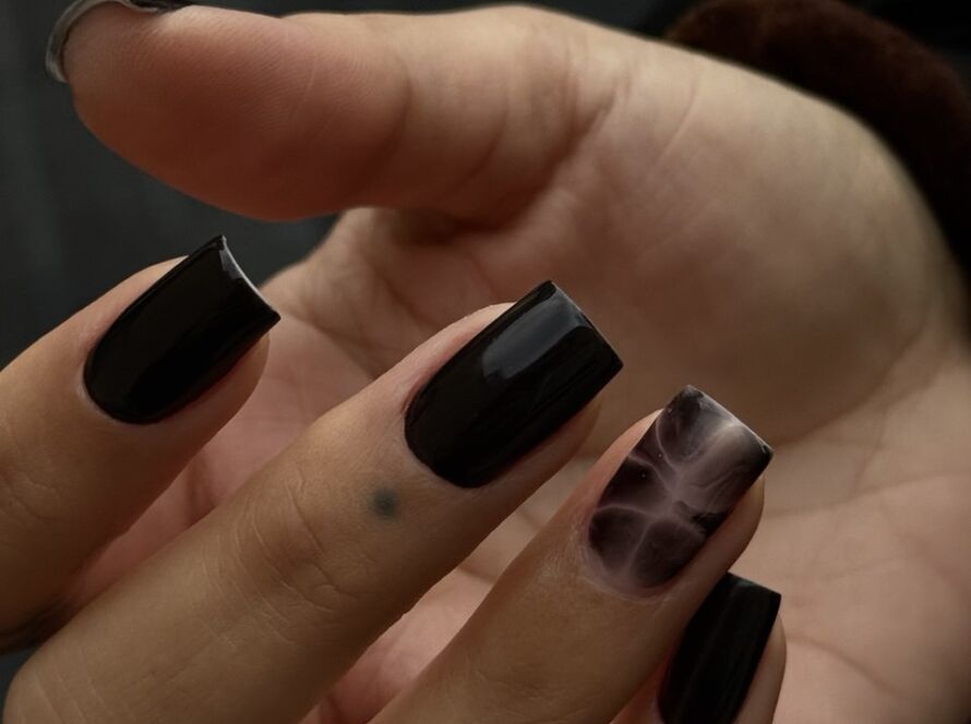 Short square black gel nails with a glossy finish and a smoky marble accent nail, done using the Russian manicure technique.