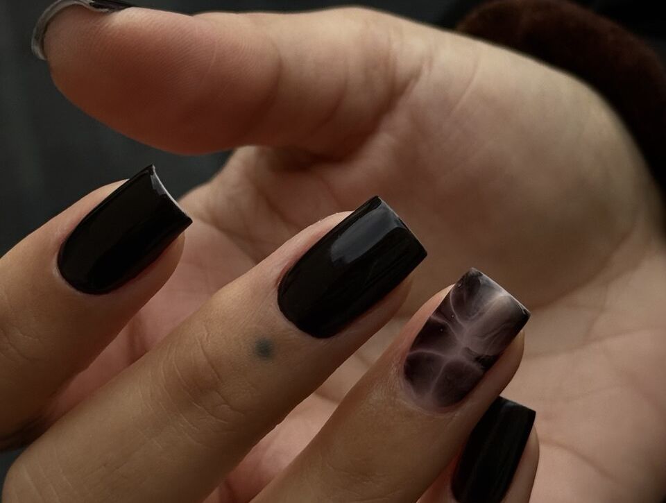 Short square black gel nails with a glossy finish and a smoky marble accent nail, done using the Russian manicure technique.