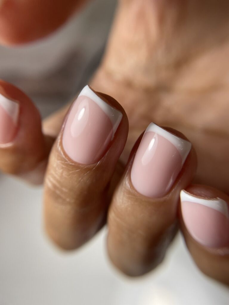 Close-up of square-shaped nails with classic French manicure featuring soft pink base and white tips in glossy finish