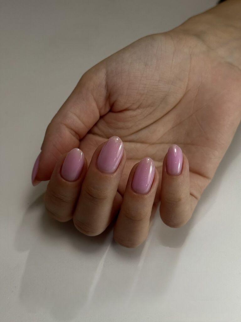 Hand displaying short almond-shaped nails with Russian manicure and glossy mauve-pink gel polish against neutral background