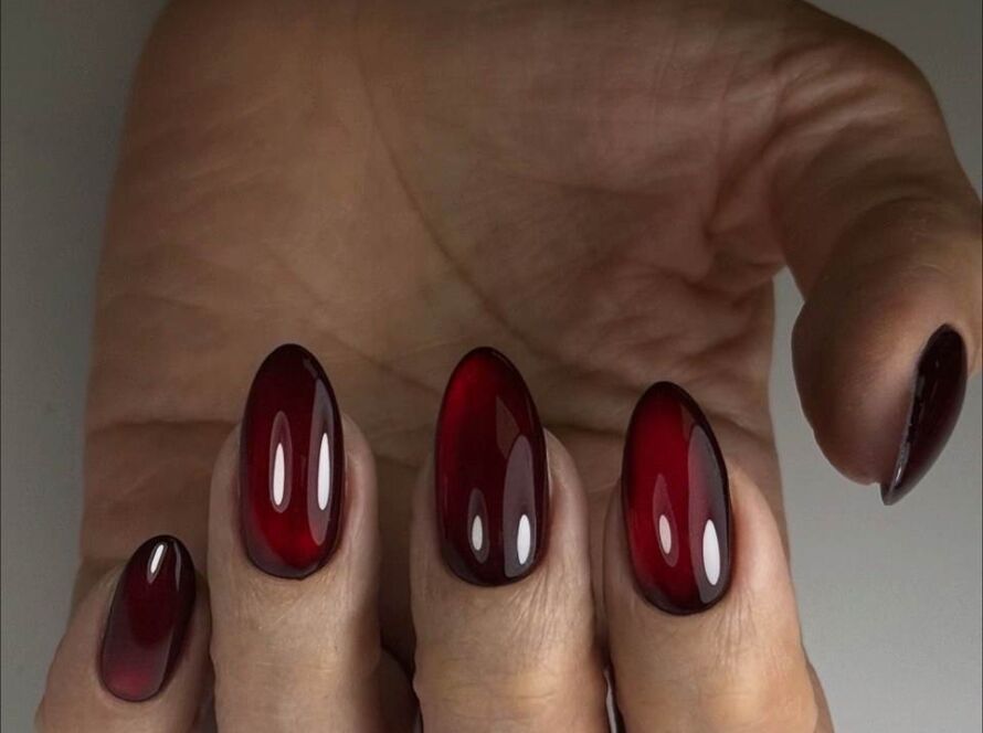 Hand displaying medium oval-shaped nails with Russian manicure featuring glossy red to burgundy ombré gradient with seamless blend against neutral background
