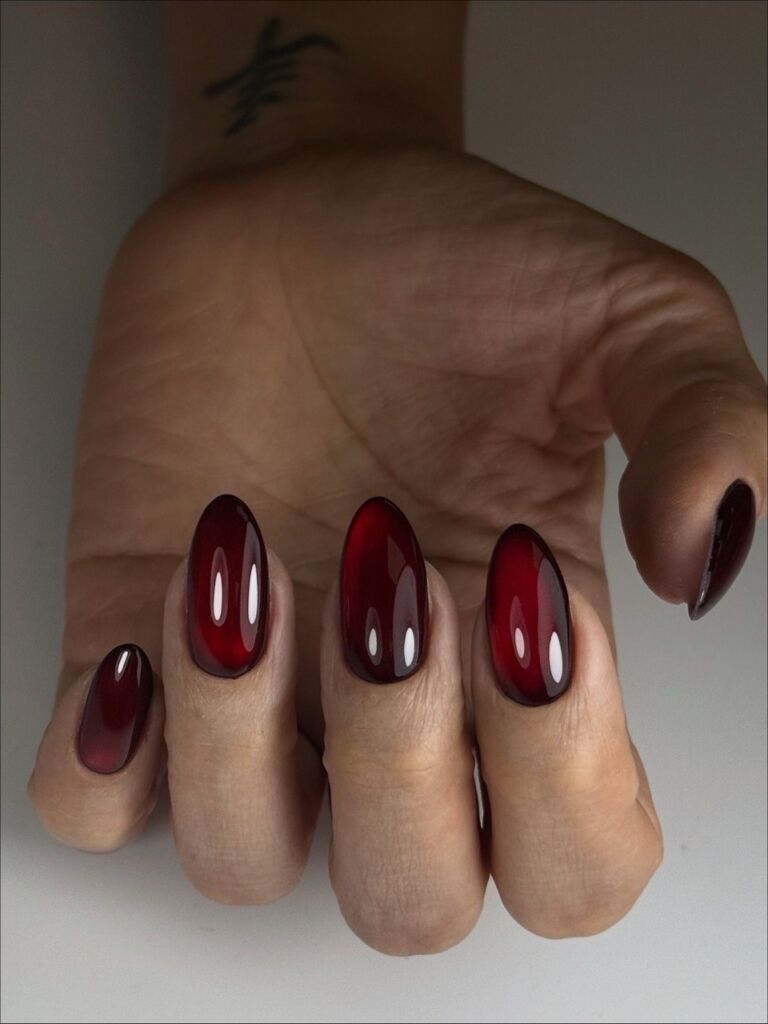 Hand displaying medium oval-shaped nails with Russian manicure featuring glossy red to burgundy ombré gradient against neutral background