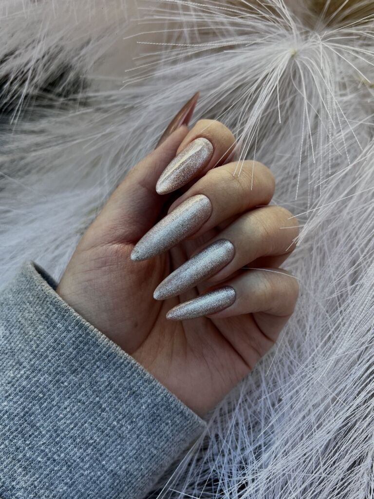Hand displaying long almond-shaped nails with Russian manicure and silver holographic glitter finish against white feathery background