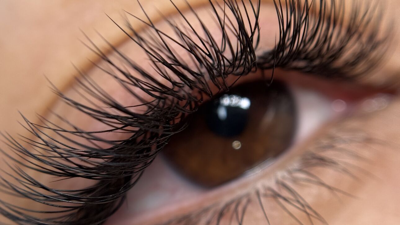 Macro view of a brown eye with full, curled lash extensions, highlighting the volume and length of the lashes along the upper lash line.