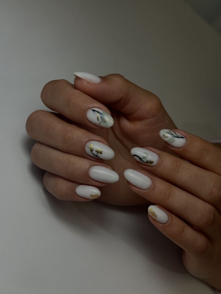 Soft minimalism with delicate details. White nails with fine botanical designs and subtle gold accents - elegance in every touch.
