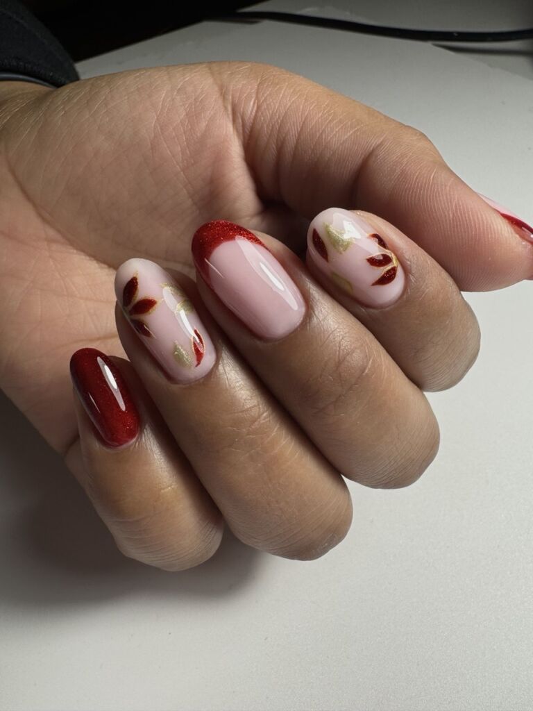 Close-up of glossy red and soft pink nails with gold leaf accents and delicate leaf nail art.